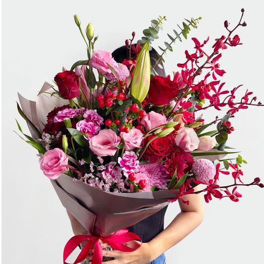 A vibrant celebration of love and joy, this bouquet features radiant roses, carnations, tulips, daisies, lisianthus, wax flowers, and silver dollar eucalyptus. In bold red and pink tones, it bursts with lively charm and heartfelt warmth.