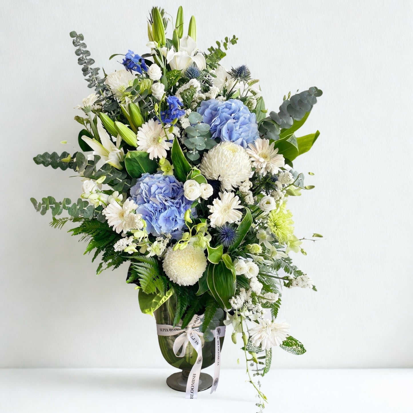 Elegant and serene, this bouquet features a dreamy combination of hydrangeas, daisies, lilies, roses, carnations, orchids, and silver dollar eucalyptus. In calming whites with contrasting blue accents, it evokes peace, purity, and timeless sophistication.