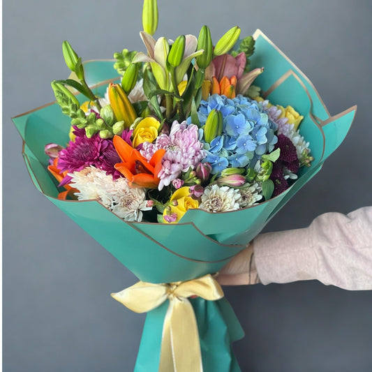 A beautiful blend of hydrangeas, daisies, chrysanthemums, lilies, lisianthus (eustoma), and carnations, complemented by fresh green leaves. This bouquet offers a harmonious mix of colors and textures, creating a refined and graceful arrangement perfect for any occasion.