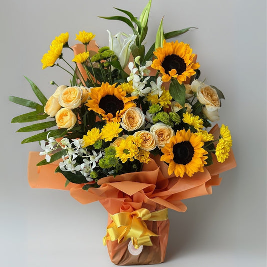 A radiant bouquet of sunflowers, roses, daisies, and lilies, with vibrant yellow hues and fresh green accents. This arrangement brings the warmth of sunshine and the elegance of classic blooms together, perfect for brightening any occasion.