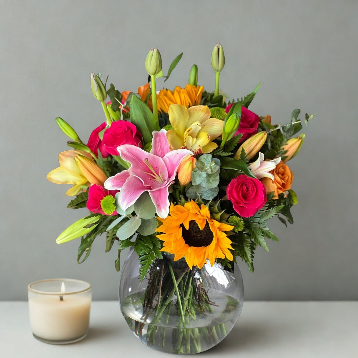 A stunning blend of sunflowers, lilies, lisianthus (eustoma), and carnations, elegantly accented with eucalyptus and lush green leaves. This radiant bouquet exudes warmth, grace, and charm, making it a perfect gift to brighten any occasion with beauty and joy.