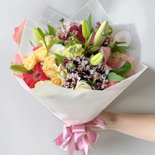 A captivating mix of timeless roses, elegant lilies, delicate lisianthus, and cheerful daisies, this arrangement radiates grace and charm. The soft petals and refreshing hues create a breathtaking floral experience, perfect for any celebration.