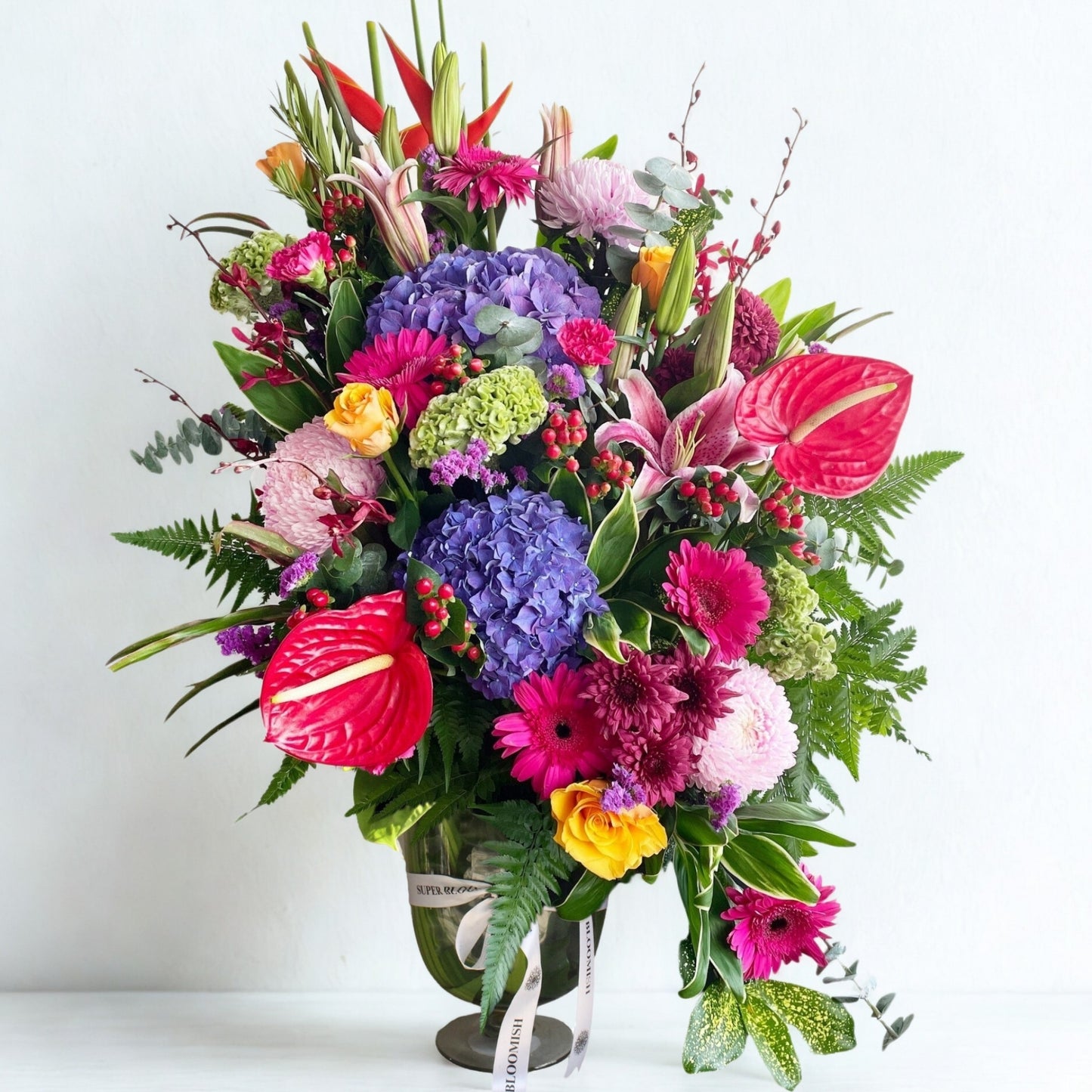 A stunning burst of nature’s finest, this vibrant bouquet blends anthurium, hydrangea, daisies, lilies, heliconia, roses, green fillers, and silver dollar eucalyptus. A rich mix of textures and multicolor tones, it’s crafted to dazzle and delight with every glance.