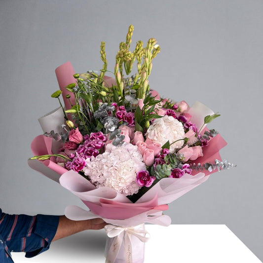 This exquisite bouquet features a stunning combination of Hydrangeas, Roses, Tuberoses, Carnations, Green Buttons, and Eucalyptus, each element carefully chosen to create a harmonious blend of color, texture, and fragrance.