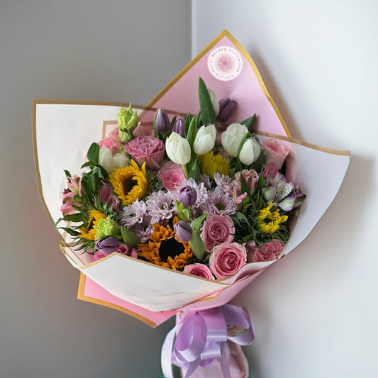 A vibrant and cheerful bouquet combining the elegance of roses, the grace of lilies, the softness of lisianthus, and the sunshine of sunflowers and tulips. This arrangement bursts with color, creating an uplifting and joyful display.