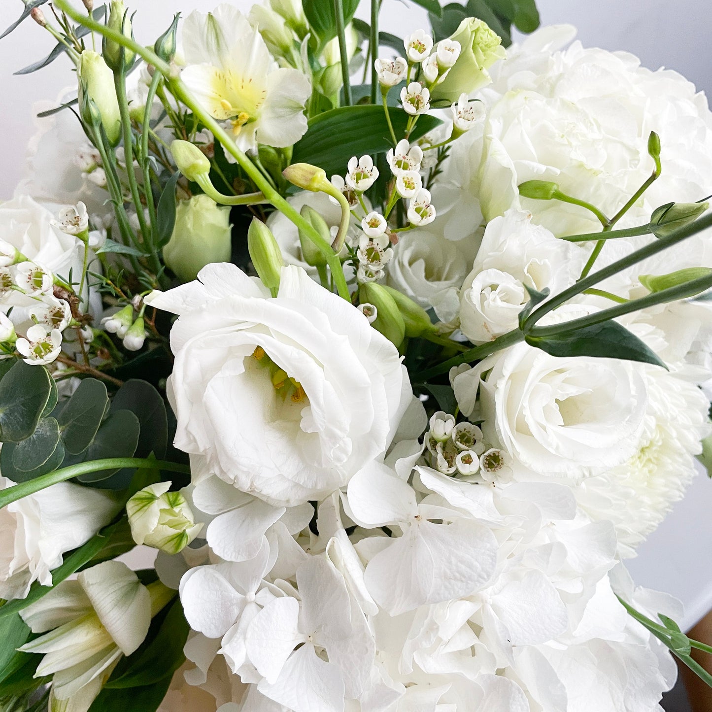 A serene and sophisticated arrangement in a pure white palette, featuring white hydrangeas, carnations, eustoma (lisianthus), wax flowers, and silver dollar eucalyptus. This bouquet radiates elegance, peace, and timeless beauty—perfect for heartfelt occasions or serene spaces.