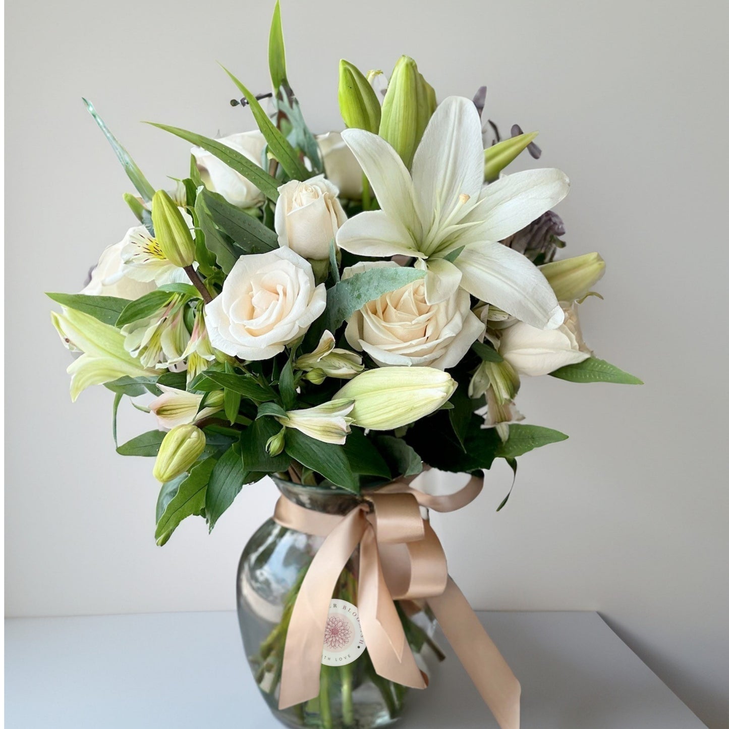 A timeless and sophisticated arrangement of pristine white lilies and delicate white roses, beautifully displayed in a chic vase. This elegant combination exudes purity, grace, and serenity, making it the perfect centerpiece for any space or a heartfelt gift for special occasions.
